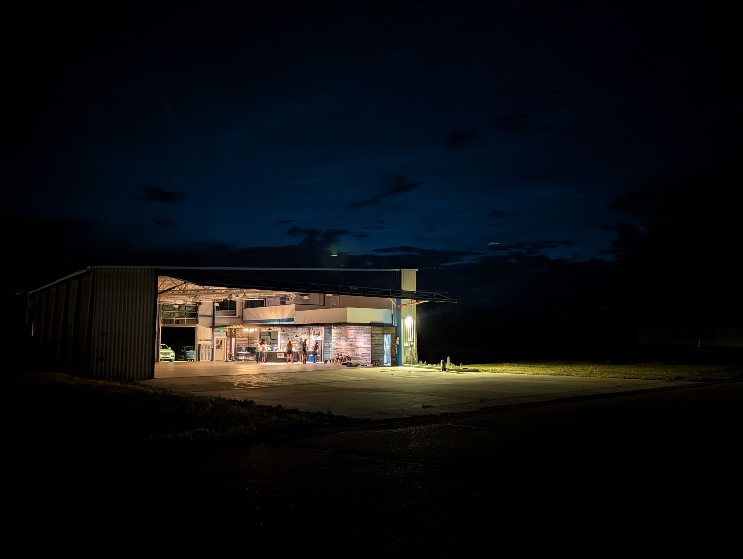 The building after dark, lit from within, alone across the slab.