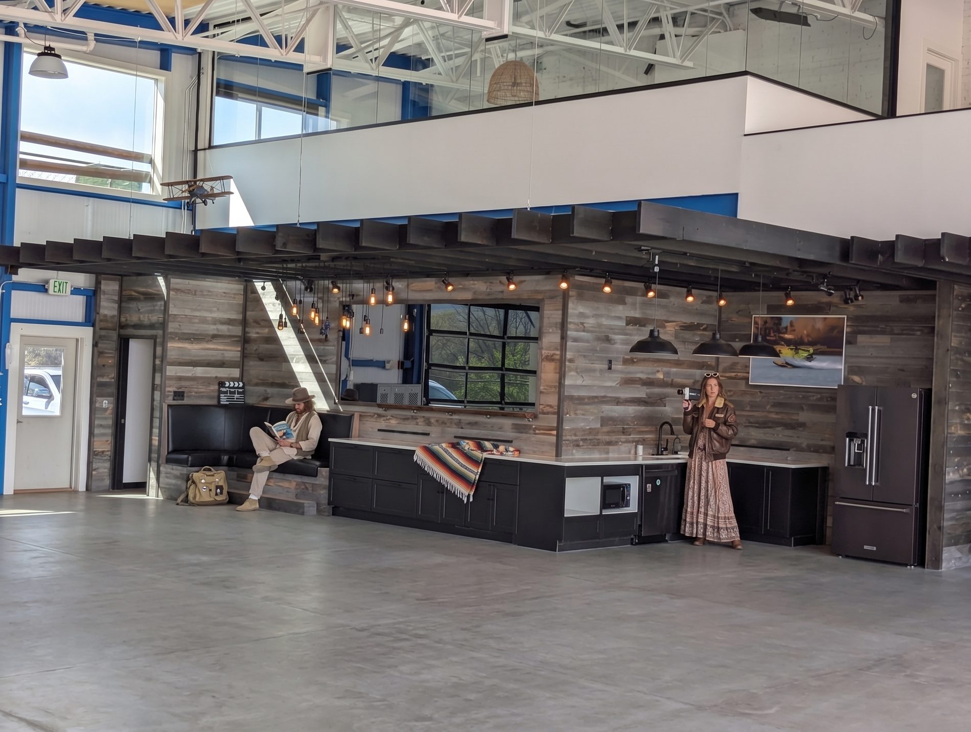 The interior: concrete floor, timber bar and kitchen, mezzanine above, two people at the counter.