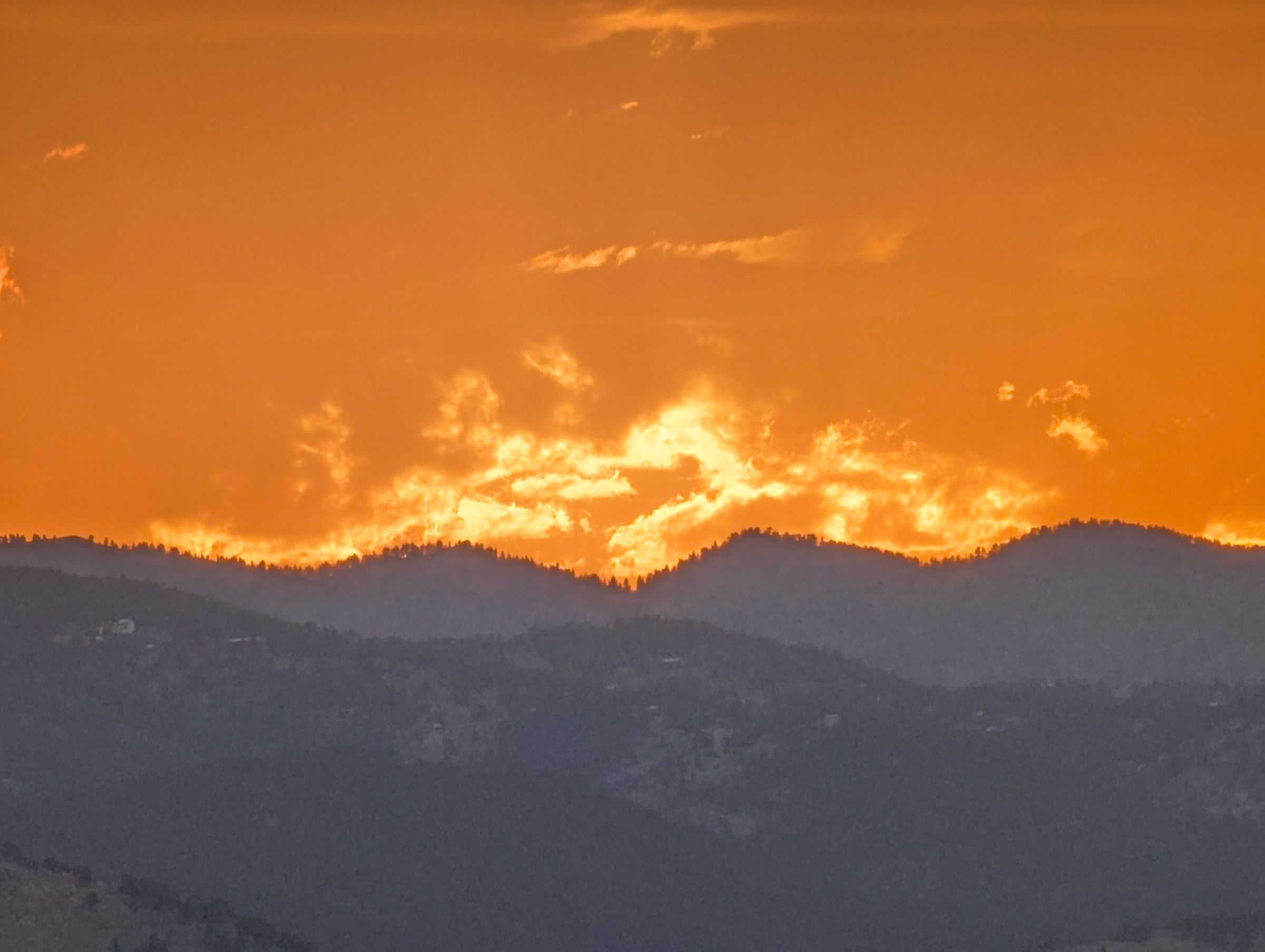 Close view of the sun going down through cloud above a forested ridge.